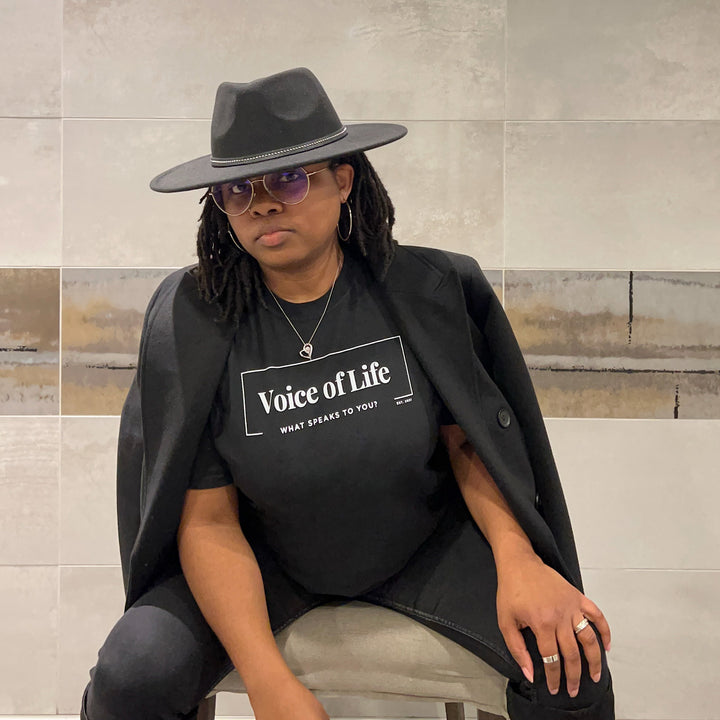 Model in black fedora and signature tee and long coat